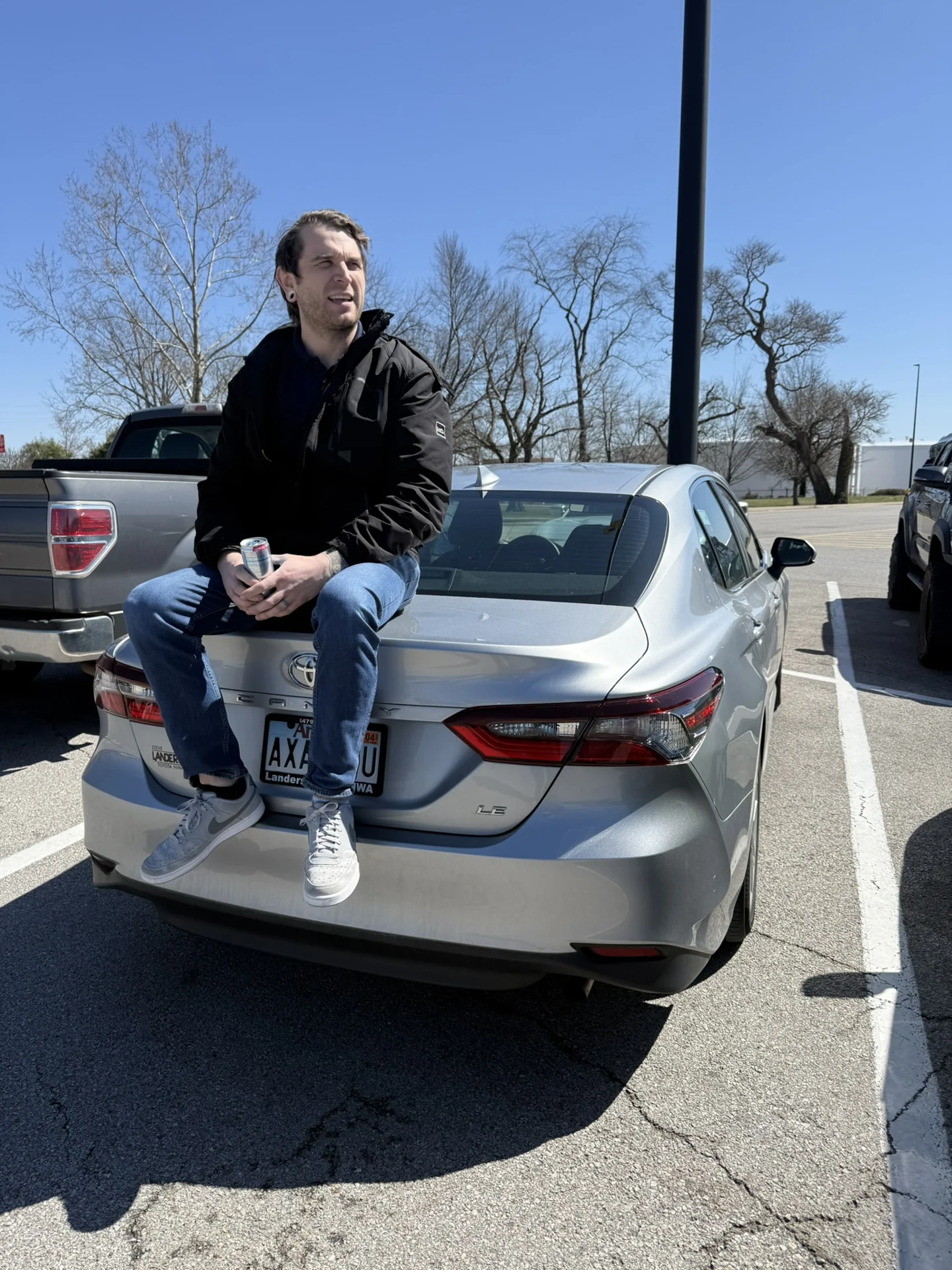 Evan Hall seated on the rear of a silver car